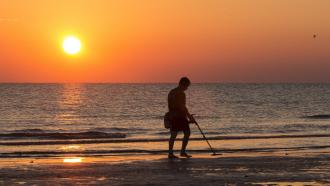 guy with metal detector on a beach at sunset